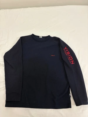 Mörkblå tröja från Vision Street Wear - Snygg mörkblå tröja från Vision Street Wear med röd broderad logga framtill. Tröjan har en klassisk rund halsringning och är tillverkad i ett mjukt material som passar perfekt till en avslappnad streetstyle-look.