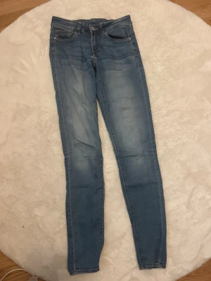 Blå skinny jeans från Divided H&M - Säljer ett par ljusblå skinny jeans från Divided H&M i storlek 34. Jeansen har klassisk femficksdesign, normal midja och smal passform hela vägen ner. Perfekta till en avslappnad stil och lätta att matcha med olika toppar.