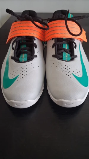Savaleos Weightlifting  Nike sneakers  - Snygga sneakers från Nike i vitt med turkosa detaljer och en stor orange rem över vristen. Skorna har svarta snören, svart innersula och en unik sula med transparent detalj på hälen. Perfekta för dig som vill sticka ut med färg och stil. Denna skor är använd 3 gånger så det är helt nya.