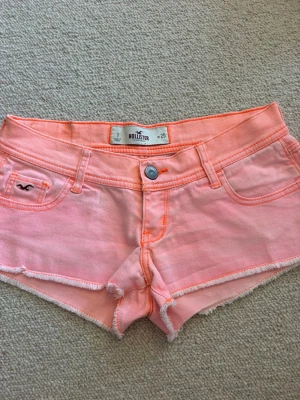 Ljusrosa shorts från Hollister - Snygga ljusrosa shorts från Hollister med råa kanter och klassisk femficksdesign. Shortsen har orangea sömmar och detaljer samt en liten logga på fickan fram. Perfekta för varma dagar och har en avslappnad, trendig look.💓
