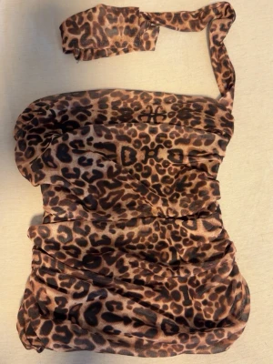 Leopardmönstrad bandeau tubtopp - Säljer en leopardmönstrad bandeau topp med draperad design och ett ihop sytt matchande band. Toppen har en snygg offshoulder-look och är perfekt för dig som vill sticka ut. Materialet känns lätt och stretchigt, vilket gör den bekväm att bära.