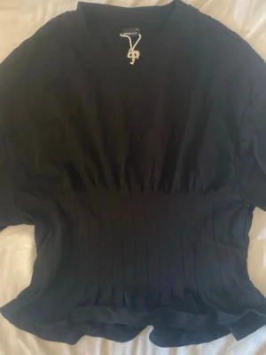 Svart ribbad topp med kort ärm - En svart topp med ribbad midja och korta ärmar. Toppen har en enkel, stilren design och rund halsringning. Perfekt att matcha med jeans eller kjol för en clean look.