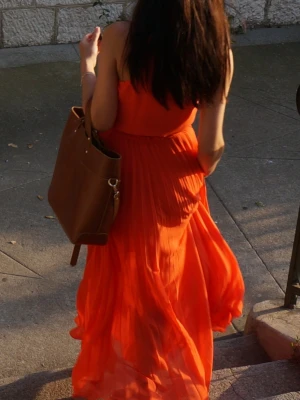 Lång orange plisserad klänning från Michael Kors - Säljer en väldigt fin och elegant klänning från Michael Kors som jag fått många komplimanger för. Den  har en ärmlös design och markerad midja, vilket ger en snygg siluett. Perfekt för sommar. Den är sparsamt använd, men har ett vitt märke med två små hål i kjolens vek som inte syns när man har klänningen på, se bilderna. Tillhörande bältet finns inte kvar men den kan bäras utan eller något annat passande.