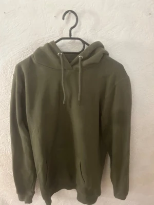 Grön hoodie från 157 - Säljer en grön hoodie från 157 med klassisk huva och dragsnören. Hoodien har en enkel och clean design med fickor framtill och ribbade muddar vid ärmar och nederkant. Perfekt för en avslappnad och stilren look.