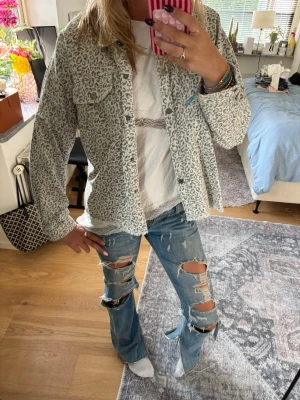 Grå leopardmönstrad jeansjacka - Säljer en grå jeansjacka med leopardmönster. Jackan har klassisk krage, knäppning framtill och två bröstfickor. Perfekt för dig som vill sticka ut med en trendig och cool look. Långärmad och i avslappnad passform.