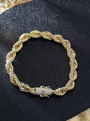 14k guldpläterad cordell armband - Säljer ett snyggt armband i guldfärgad metall med tvinnad design. Låset är dekorerat med små gnistrande stenar som ger extra bling. Perfekt för dig som gillar statement-smycken och vill sticka ut lite extra.