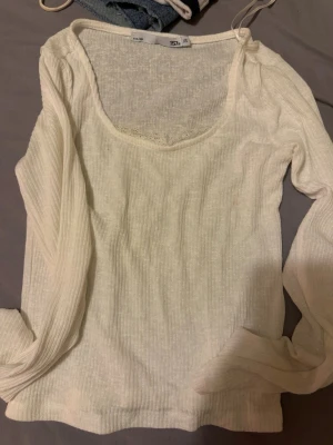 Vit ribbad långärmad topp lager 157 - Säljer en vit ribbad långärmad topp från 157 i storlek XS. Toppen har en djup, rundad ringning och är tillverkad i ett mjukt, stretchigt material som sitter snyggt på kroppen. Perfekt att styla med jeans eller kjol.
