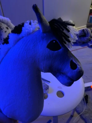 Käpphäst med svartvit man - Säljer en hemmagjord käpphäst med mjuk, ljusgrå plysch och svartvit man av garn. Hästen har broderade svarta detaljer för ögon och näsborrar samt svarta fläckar på huvudet. Perfekt för dig som gillar hästar och vill ha något unikt!