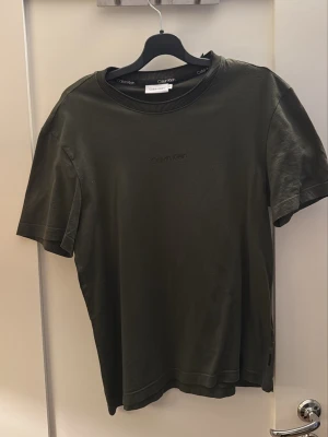 Mörkgrön Calvin Klein t-shirt - Snygg mörkgrön t-shirt från Calvin Klein med diskret logga broderad på bröstet. Klassisk rund halsringning med ribbad kant och korta ärmar. Tillverkad i mjuk bomull för en skön känsla och enkel stil.