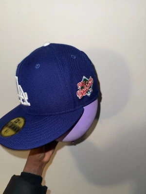 Blå LA Dodgers keps New Era - Säljer en blå LA Dodgers keps från New Era med broderad vit LA-logga framtill och 1981 World Series patch på sidan. Klassisk flat brim och strukturerad passform. Perfekt för dig som gillar sportig streetstyle.