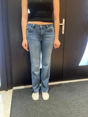 Blå bootcut jeans med fickdetaljer - Säljer ett par klassiska blå bootcut jeans med snygga fickdetaljer bak och låg midja. Jeansen har en lätt tvättad look och raka ben som går ut lite nertill. Perfekta till sneakers eller boots för en chill stil.