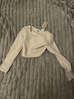 Ljusbeige croppad långärmad topp H&M - Säljer en ljusbeige croppad långärmad topp från H&M Sport. Toppen har rund halsringning och är tillverkad i ett mjukt, stretchigt material. Är ej säker helt på färg men vit/beige 