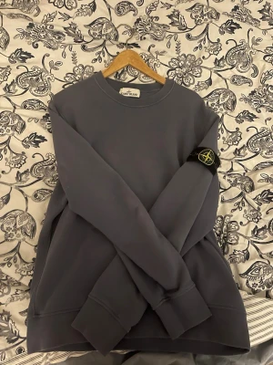 Grå sweatshirt från Stone Island - Säljer en stilren grå sweatshirt från Stone Island med klassisk rund hals och ikonisk logotyp-patch på ärmen. Tröjan är i mjukt material och har ribbade muddar vid ärmslut och nederkant. Perfekt för en avslappnad och trendig look. PRIS KAN DISKUTERAS VID SNABBT KÖp