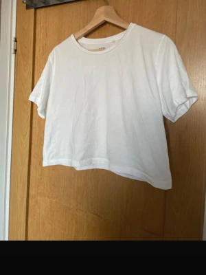 Vit croppad t-shirt från 157 - Säljer en enkel och fräsch vit croppad t-shirt från 157 i storlek L. T-shirten är tillverkad i 100% bomull och har korta ärmar samt en klassisk rund halsringning. Perfekt basplagg till garderoben!