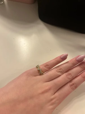 Guldfärgad ring med stenar - Snygg guldfärgad ring med flera runda, klara stenar i rad. Ringen har en enkel men elegant design som passar perfekt för dig som gillar stilrena accessoarer. Materialet ser ut som metall med glittrande stenar som ger en lyxig känsla.