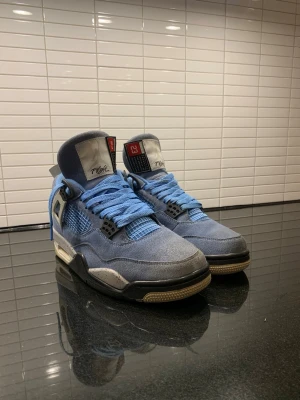 Air Jordan 4 University Blue sneakers - Snygga Air Jordan 4 University Blue sneakers med ljusblå mocka, svarta och vita detaljer samt blå skosnören. Ikonisk Jumpman-logga på sulan och meshpaneler på sidorna. Högt skaft och klassisk retrostil som sticker ut.