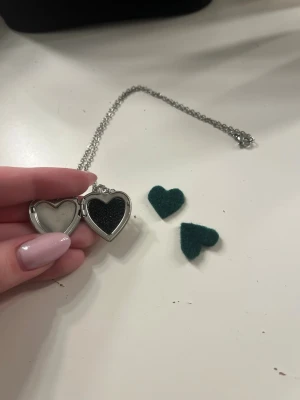 Silverfärgat hjärthalsband (parfym) - Snyggt halsband med ett blankt, silverfärgat hjärthänge i metall. Kedjan är tunn och enkel, vilket gör att hjärtat verkligen står ut. Perfekt accessoar för att ge din outfit en romantisk touch. Spraya parfym på tyghjärtat och placera de i hjärtat så doftar de av din parfym längre!!