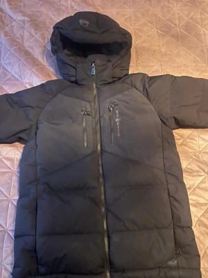 Sail racing jacka till vinter - Snygg svart dunjacka till vinter den är typ inte använd jag har använt den typ nio gånger för den blev för liten på mig den är helt ny och den är inte trasig nånstans plus den är äkta. Det finns tre lågor på jackan en på armen en på brösten och en på luvan hoppas du blir intresserad av jackan.