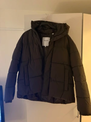 Svart pufferjacka från Jack & Jones - Säljer en svart pufferjacka från Jack & Jones i storlek M. Jackan har en hög krage, dragkedja framtill och stora fickor på sidorna. Perfekt för kalla vinterdagar med sin vadderade design och klassiska look.