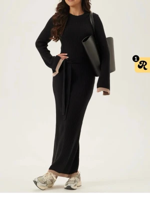 Svart klänning från bubblerrom - svart ribbstickad långklänning. Tillhörande midjebälte för en markerad siluett. 