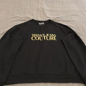 Versace Jeans Couture Sweatshirts - Svart sweatshirt från Versace Jeans Couture med guldfärgad logotyp framtill. Tillverkad i 100% bomull med normal passform.  Endast använd några få gånger och i mycket bra skick.