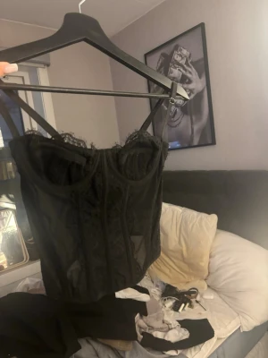 Svart spetskorsett från SHEIN - Trendig svart korsett från SHEIN med tunna axelband och detaljer i spets. Modellen har markerade sömmar och meshpartier som ger en snygg siluett. Perfekt för dig som vill ha en edgy och feminin look. Materialet är en mix av spets och mesh.