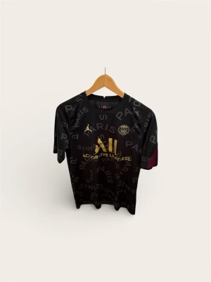 PSG x Jordan Matchtröja (Stl M) – Svart/Guld - Säljer en riktigt snygg Paris Saint-Germain matchtröja från det populära samarbetet med Jordan Brand. Svart bas med "PARIS"-mönster och exklusiva detaljer i guld (loggor och sponsor).  En tröja som funkar lika bra till vardags (streetwear) som på fotbollsträningen.  Skick: Fint begagnat skick!  Storlek: Medium (M).  Pris: 399 kr 