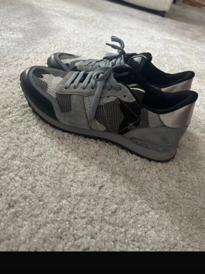 Grå camo sneakers från Valentino - Snygga sneakers från Valentino i grått camomönster med detaljer i mocka och mesh. Skorna har svarta och silverfärgade inslag, rund tå och klassisk snörning. Perfekta för dig som vill ha en unik och trendig look.