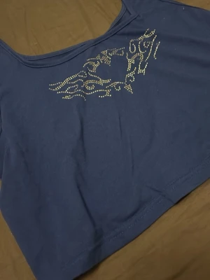 Blå croppad topp med strasstenar - Snygg blå croppad topp med ett coolt mönster av strasstenar framtill. Toppen har en bred halsringning och är ärmlös, perfekt för att styla med höga jeans eller kjol.