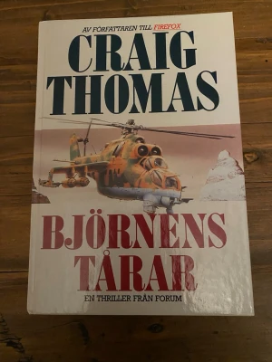Björnen tårar av Craig Thomas - En spännande thrillerbok av Craig Thomas med titeln 'Björnen tårar'. Omslaget är vitt med en illustration av en militärhelikopter och snötäckta berg. Inbunden.