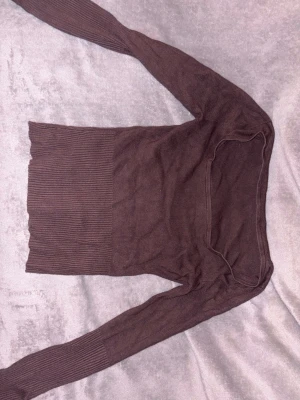 Brun ribbstickad tröja - Mörkbrun ribbstickad tröja med lång ärm och bred, rundad halsringning. Tröjan har en smal passform och är tillverkad i ett mjukt, stretchigt material som sitter snyggt på kroppen.