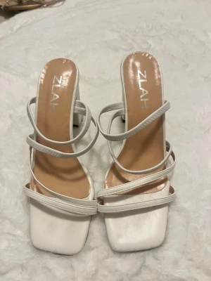 Vita sandaler med blockklack  - Säljer ett par trendiga vita sandaler från med fyrkantig tå och flera tunna remmar. Sandalerna har en stabil blockklack och öppen häl. Materialet ser ut att vara konstläder med en matt finish. Sjukt bekväma. 