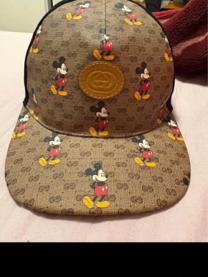 Gucci x Disney Mickey Mouse keps - Snygg keps från Gucci i samarbete med Disney, täckt av Mickey Mouse-motiv på brun canvas med GG-mönster. Kepsen har svart mesh baktill och ett brunt lädermärke framtill. Perfekt för dig som gillar streetwear och unika accessoarer.  Storlek xl/L  59-60 cm helt ny aldrig använd  100% äkta pris kan diskuteras tar emot byte mot gucci väska elle skor med tigerprint (äkta) 