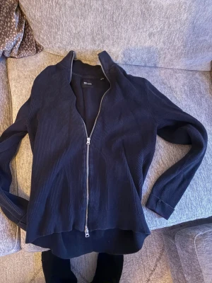 Mörkblå ziptröja  - Säljer en svart ribbad ziptröja från H&M med hel dragkedja framtill och hög krage. Tröjan har långa ärmar och är tillverkad i ett mjukt, stretchigt material som passar perfekt till en avslappnad stil.