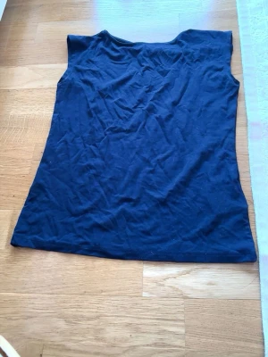 Mörkblå ärmlös linnetopp - En enkel och stilren mörkblå linnetopp i mjukt bomullsmaterial. Toppen är ärmlös och har en rak passform, perfekt att matcha med jeans eller kjol. Inga synliga detaljer eller mönster, bara clean och basic.