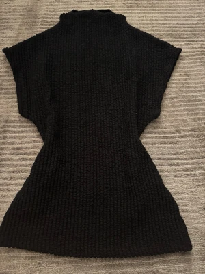 Svart stickad topp från Gina Tricot - Säljer en svart stickad topp från Gina Tricot i storlek XS. Toppen har en hög hals, korta ärmar och är ribbstickad för en snygg och figurnära passform. Perfekt att styla med jeans eller kjol för en trendig look.