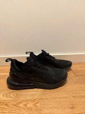 Nike Air Max 270 helsvarta sneakers - Snygga helsvarta Nike Air Max 270 sneakers med mesh-ovandel och stor synlig Air-enhet i hälen. Skorna har en sportig siluett, diskreta swoosh-loggor och dragflik bak. Perfekta för dig som gillar stilrena och bekväma sneakers.