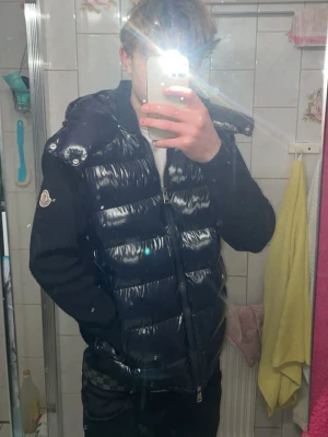 Mörkblå cardigan från Moncler - Säljer en mörkblå cardigan från Moncler med glansig finish och huva. Jackan har långa ärmar i mjukt material och klassisk Moncler-logga på ärmen. Dragkedja framtill och quiltad design som ger en modern look.