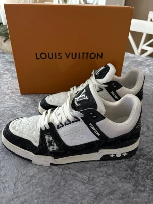 Louis Vuitton svartvita sneakers - Snygga Louis Vuitton sneakers i svart och vitt med klassiska LV-loggor på plösen och sidan. Skorna har en låg siluett, vita snören och detaljer i präglat läder samt textil. Perfekta för dig som vill sticka ut med stilrena skor. Storlek 44 men passar också 43. Använda ett fåtal gånger, bara att skicka och fråga om det är något 