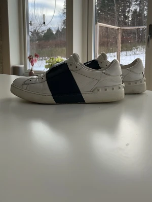 Valentino Open  vit/marinblå - Snygga Valentino Open sneakers i vitt skinn med bred marinblå rem över vristen. Skorna är i storlek 42 men passar lite även lite större. Bra skick, inga större defekter
