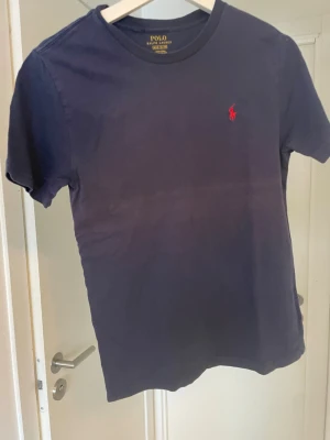 Mörkblå t-shirt från Polo Ralph Lauren - Snygg mörkblå t-shirt från Polo Ralph Lauren. Tröjan är i ett mycket bra sick. Storlek: 10-12/ 150cm.