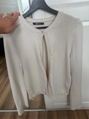 Beige kofta från Gina Tricot - Säljer en enkel och stilren beige kofta från Gina Tricot. Koftan har rund halsringning, lång ärm och stängs med en knapp upptill. Materialet är mjukt och stickat, perfekt för lager på lager och en clean look.