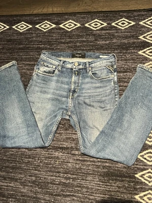 Blå Replay jeans  - Säljer ett par klassiska blå jeans från Replay, modell Thad. Jeansen har raka ben, fem fickor och snygga slitningar för en avslappnad look. Tillverkade i mjuk denim med Replay-logga på myntfickan och metallknapp i midjan.