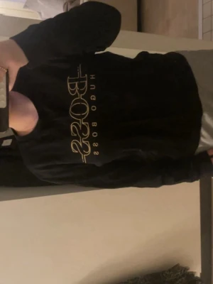Svart sweatshirt från Hugo Boss - Svart sweatshirt från Hugo Boss med stort guldfärgat BOSS-tryck på bröstet. Tröjan har rund halsringning och är i slim fit-modell. Perfekt för en clean och stilren look.