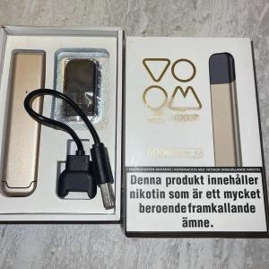 VOOM Starter Kit e-cigarett guld - VOOM Starter Kit innehåller en guldfärgad e-cigarett, USB-laddningskabel och en ny oöppnad pod . levereras i originalförpackning och är enkel att använda för nikotinintag. Modern och stilren design.