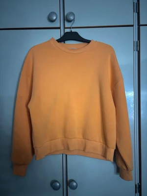 Oversized orange sweatshirt - En oversized orange sweatshirt med rund hals och ribbade muddar vid ärmslut och nederkant. Tröjan har en enkel och clean design utan tryck eller logga, perfekt för en chill och avslappnad stil. Materialet känns mjukt och bekvämt, passar perfekt till jeans eller mjukisbyxor.