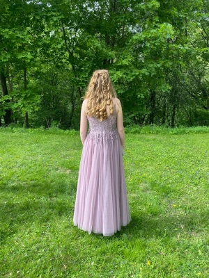 Ljuslila balklänning med spetsdetaljer - Elegant ljuslila klänning med v-ringning och tunna axelband. Överdelen har vackra spetsdetaljer. Perfekt för speciella tillfällen. Frakt ingår.