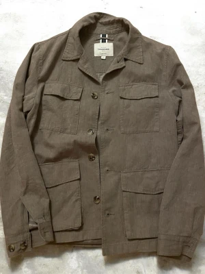 Brun overshirt från Drakes - Letar du efter en jacka/overshirt till våren då är denna perfekt 🔅Stilren brun overshirt från Dreasman i ett lätt linnematerial. Klassisk krage, fyra stora fickor framtill och knäppning med bruna knappar. Perfekt lager på lager-plagg med avslappnad passform och snygga detaljer. 