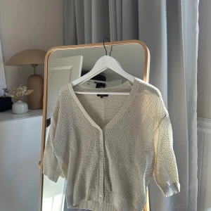 Beige kofta (guldskimrande) - Säljer en beige kofta med v-ringning och knappar framtill. Koftan har en avslappnad passform, trekvartsärmar och är stickad i ett mjukt material. Den har ett guldigt skimmer. Aldrig använd. Står xs på lappen men passar mig som har S/M