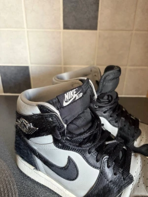 Nike Air Jordan 1 High svart/grå - Unika Nike Air Jordan 1 High sneakers i svart och grått med detaljer i konstläder och pälsliknande material. Klassisk hög siluett med svart swoosh, svarta skosnören och Air Jordan-logga på sidan. Perfekta för dig. Köpta för ungefär 2000 kr och säljer för 800 då dom är använda en del💞Det är inga defekter på skorna förutom en liten plast/gummiparti på sulan som åkt bort . kan skicka bild privat för dom som vil se
